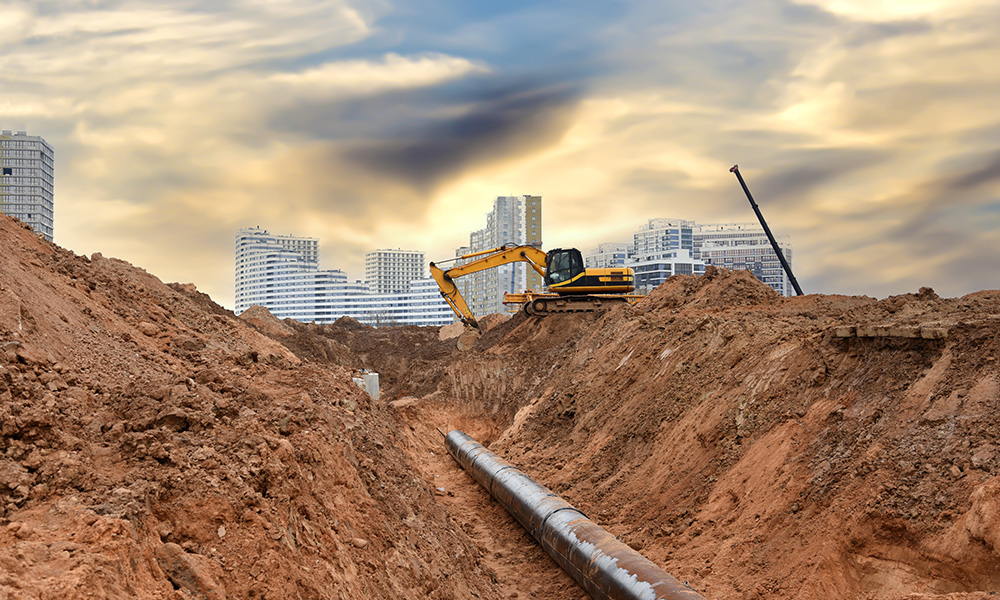 Excavator at construction site during laying sewer and main reticulation systems. Civil infrastructure pipe, water lines, sanitary sewers and storm sewers. Underground utilities installation